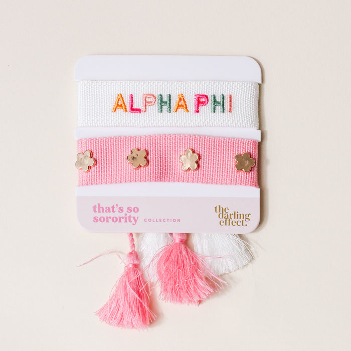 The Darling Effectβs Alpha Phi Woven Bracelet Set includes two adjustable bracelets on a cardβone white with colorful βALPHA PHIβ embroidery and one pink with gold flower studsβfinished with pink and white tassels. Perfect for sisterhood gifting!.