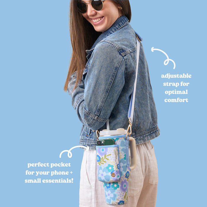A woman smiles while wearing a denim jacket and linen pants, carrying The Darling Effectโs Beyond Blooms Blue Green Tumbler Sling with a phone pocket and adjustable strap.