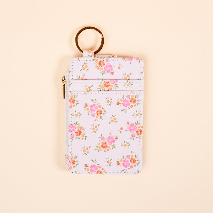 The Darling Effectβs Endless Daydream Cream Keychain Wallet is a slim, rectangular white wallet with pink and orange floral patterns, a zippered coin holder, and gold keyringβdisplayed on a light beige background.