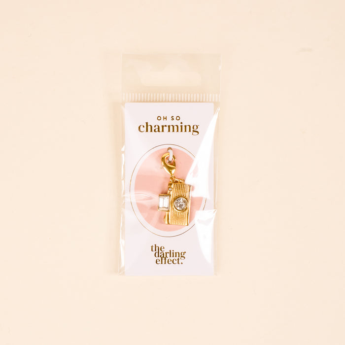 The Darling Effect Film Camera Jewelry Charm Gold features a crystal detail and comes attached to an "OH SO charming" card, packaged in a clear bagโperfect for adding to your personalized jewelry collection.
