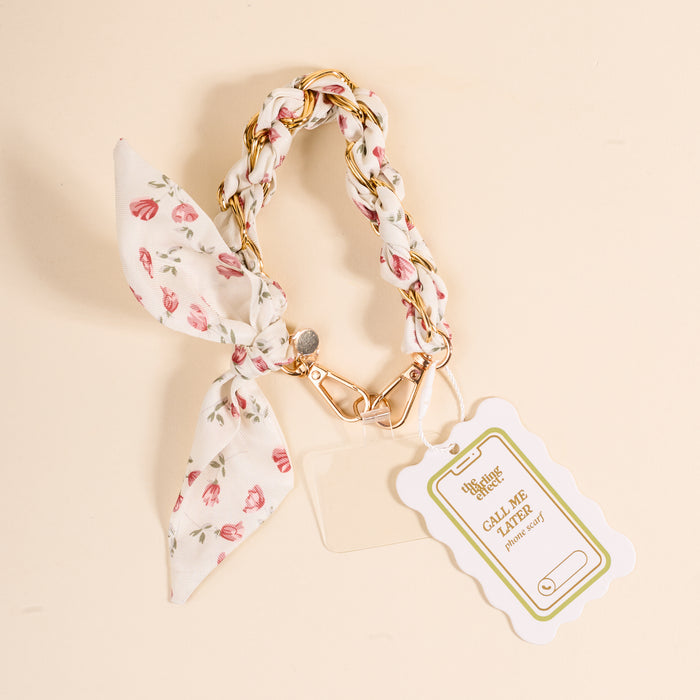 The Darling Effectβs Garden Party Call Me Later Phone Scarf is a floral keychain with a braided strap, gold clasp, and bow. On a light background, it displays a scalloped tag reading CALL ME with a phone graphic.