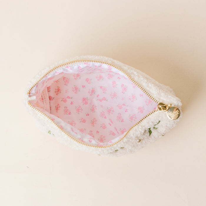 The Kappa Delta Bows & Pearls Teddy Pouch by The Darling Effect is a small white sherpa pouch with a gold zipper and pink floral liningβperfect as a cozy sorority gift. It's shown open on a light beige surface.