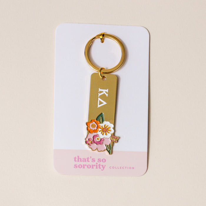 The Darling Effect's Kappa Delta Enamel Keychain features Greek letters and colorful flower designs, attached to a display card labeled "thats so sorority COLLECTION," making it an ideal gift for any Kappa Delta sister.