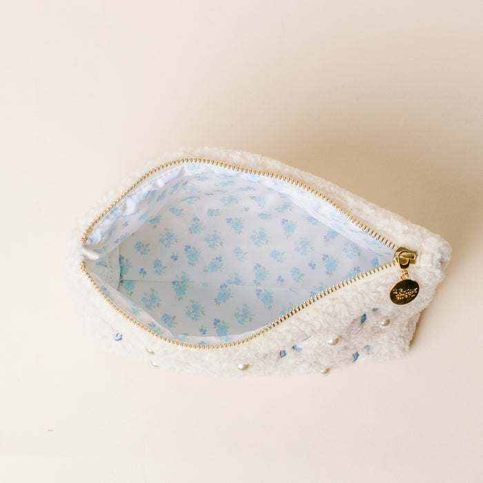 The Darling Effectβs Kappa Kappa Gamma Bows & Pearls Teddy Pouch features a soft white sherpa exterior, gold zipper with a round charm, embroidered bows, and light blue floral liningβan ideal sorority gift.