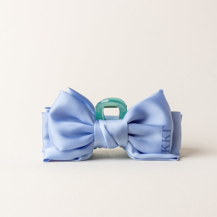 The Darling Effectβs Kappa Kappa Gamma Satin Bow Claw Clip features a large light blue satin bow with a blue-green center, perfect for updos and showcased on a plain, light background.