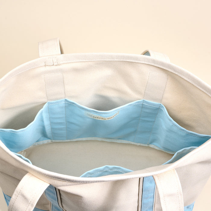 Top view of The Darling Effectβs Light Blue The Signature Canvas Tote Bag, featuring durable handles and a light blue interior with multiple compartments perfect for organizing everyday essentials.