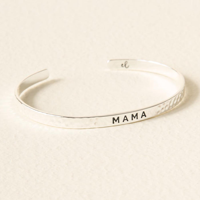 The Darling Effect Mama Cuff Bracelet features a silver hammered texture and "MAMA" engraved in black on the front, displayed elegantly on a light surface.
