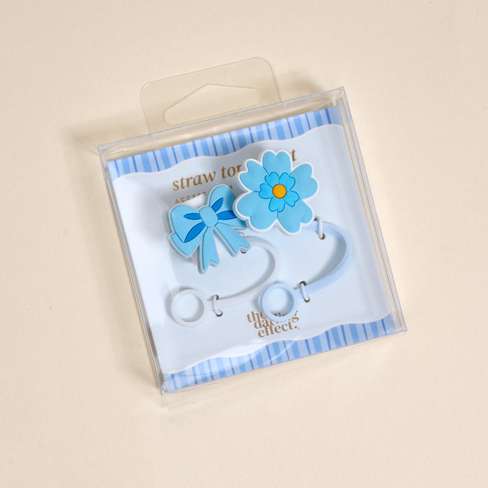 The Darling Effect's Oh So Fancy Blue Straw Topper Set includes two blue silicone toppersβa bow and a flowerβpackaged in a clear box with striped background, making your drinkware leak-resistant and stylish.