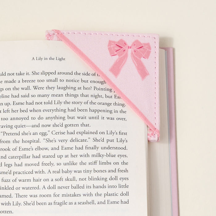 The Darling Effectโs Oh So Fancy Pink Corner Keeper Fabric Bookmark, with its stitched bow and quilted design, secures the top right corner of your pageโa thoughtful gift for book lovers, shown on a light neutral background.