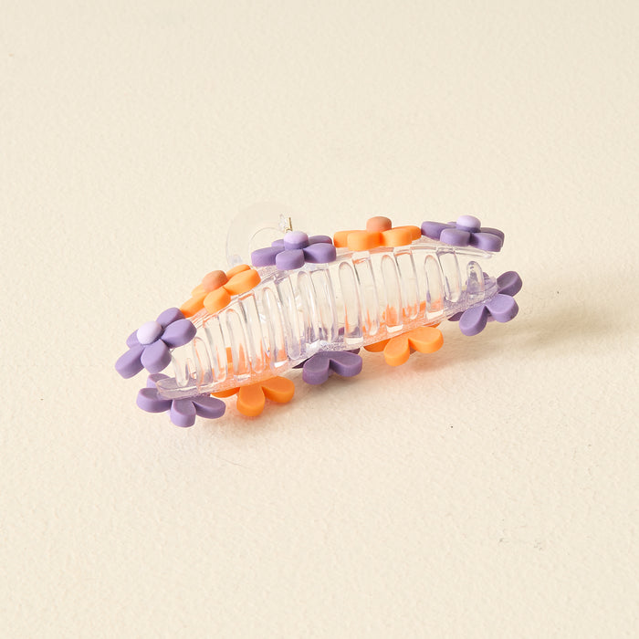 The Darling Effect's Orange Purple Game Day Daisy Claw Clip features clear plastic with purple and orange daisy accents, perfect for highlighting your school colors or adding a playful vibe on Game Day. Photographed on a light, textured background.