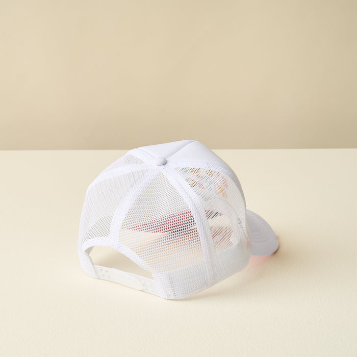 The Out of Office Trucker Hat by the-darling-effect, a white mesh-back cap with embroidered lettering, is shown upside down on a light beige surface with a matching beige background.