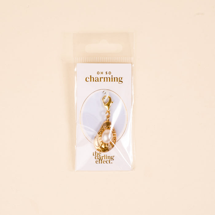 The Darling Effect's Oyster Jewelry Charm Gold keychain features a pearl charm and comes attached to an โOH SO charming & the darling effectโ card, all packaged in a clear plastic bag.