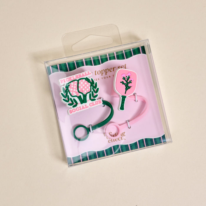 The Darling Effect Pickleball Social Club Straw Topper Set includes two silicone toppers: one green with rackets and βPICKLEBALL SOCIAL CLUB,β and one pink with a paddle and treeβfun drinkware accessories on a cream background.