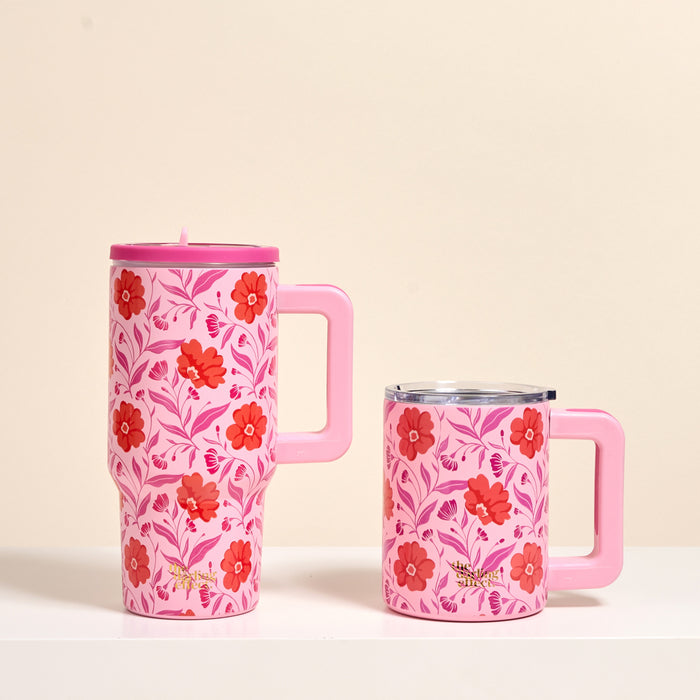 Two Poppin' Petals Hot Pink 14 oz Insulated Mugs by The Darling Effect, both with handles and a red and pink floral design, are side by side on a white surface. One is tall with a lid; the other is shorter and wider.