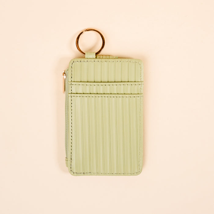 The Darling Effect's Sage Ripple Ridge Keychain Walletβa small, light green wallet with card slots, zip coin holder, vertical stitching, and a gold keyringβdisplayed on a cream background.