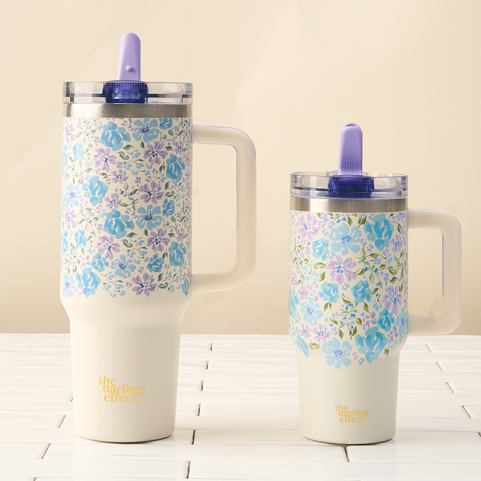 Two floral insulated mugs with handles and purple straws sit side by side on white tiles. The taller mug is the Secret Garden Blue 20 oz Lifestyle Flip Straw Tumbler by the-darling-effect, both with “the darling effect” at the bottom.