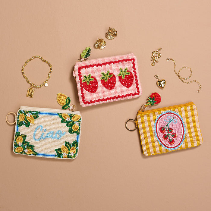 Three handcrafted beaded pouches by The Darling Effectโincluding the Strawberries Handcrafted Beaded Pouchโare shown with gold jewelry on a beige background. Each pouch is a unique accessory.