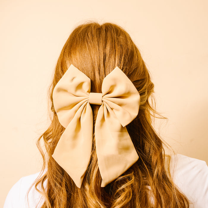 A person's back is shown with long, wavy, light brown hair adorned with The Darling Effect's Tan Hair Bowβa classic satin accessory that adds timeless charm.