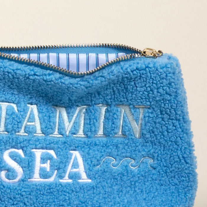 A close-up of The Darling Effect's Vitamin Sea Teddy Pouch: a blue sherpa pouch with "VITAMIN SEA" and wave embroidery, lined with blue and white stripesโan irresistibly stylish accessory.