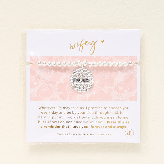 The Darling Effectβs Wifey Beaded Charm Bracelet features a silver beaded design with a circular WIFEY charm on a pink floral cardβa heartfelt gift to celebrate love.