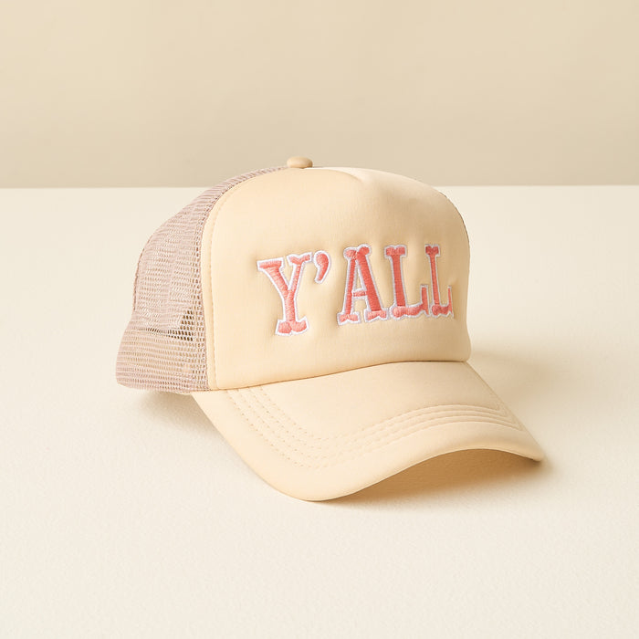 The Y'all Trucker Hat by the-darling-effect is a beige and light pink cap with mesh back panels and bold embroidered "YALL" lettering on the front, shown on a white surface with a neutral background.