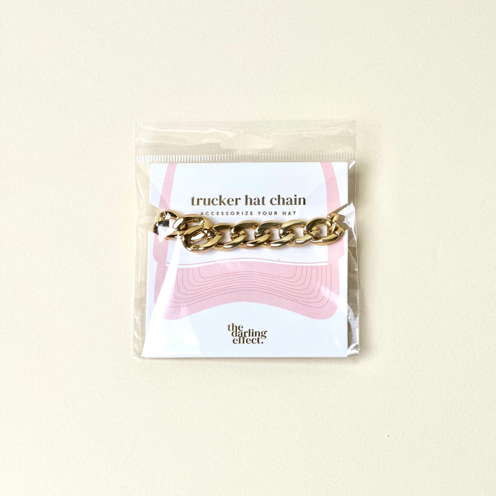 The Darling Effect Acrylic Link Gold Trucker Hat Chain shines on a light background and is packaged on a card with pink hat graphics and "the darling effect" at the bottom.