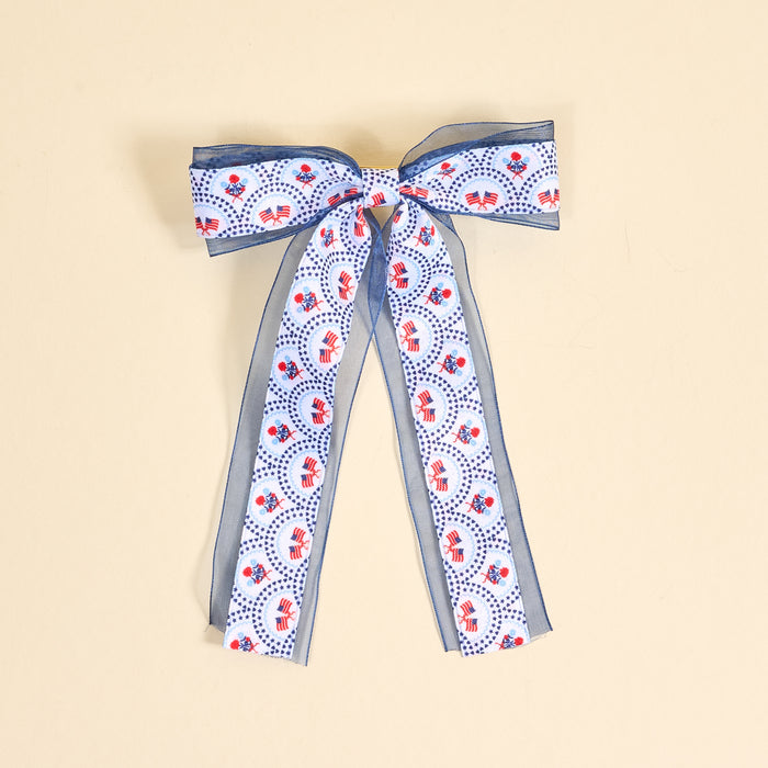The Darling Effect’s All-American Darling Lovely Layered Hair Bow features blue and white ribbons with red elephants and blue dots, adding a playful touch to your hair accessories. Shown on a beige background.