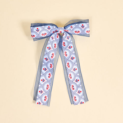 The Darling Effect’s All-American Darling Lovely Layered Hair Bow features blue and white ribbons with red elephants and blue dots, adding a playful touch to your hair accessories. Shown on a beige background.