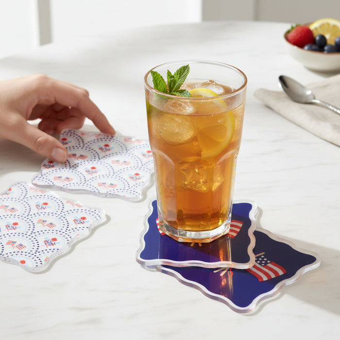 A glass of iced tea with lemon and mint rests on The Darling Effect’s All-American Darling Table Talk Acrylic Coaster, while a hand picks up another from the set nearby. A bowl of fruit and a spoon add to the inviting table décor.