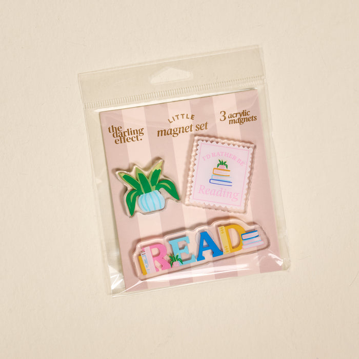 The Darling Effect’s All Booked Up Little Magnet Set includes three colorful acrylic magnets—a green potted plant, a pink “I’d rather be reading” square with books, and multicolored READ—perfect for decorating any fridge.