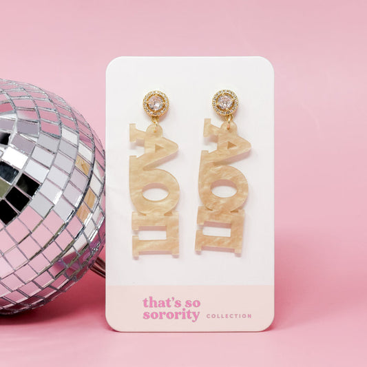 Two gold acrylic Alpha Omicron Pi letter earrings by The Darling Effect hang on a display card labeled "That's So Sorority Collection," set against a pink background—a perfect pick for bid-day baskets or sisterhood events.