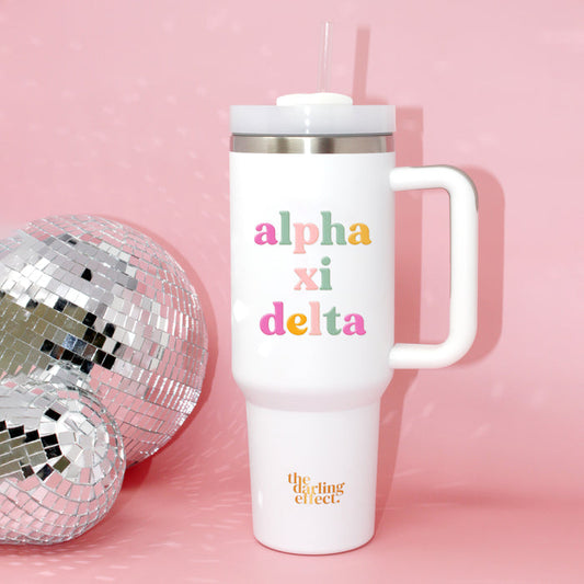 The Darling Effect Alpha Xi Delta 40 oz Take Me Everywhere White Tumbler, featuring colorful Alpha Xi Delta text and a handle with straw, sits beside a disco ball on a pink background. "The Darling Effect" is written at the bottom.