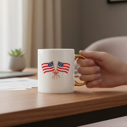 A hand holds The Darling Effect's American Flags 11 oz Cozy Cute Ceramic Mug, featuring two crossed flags and a gold handle—ideal for coffee or tea—on a desk with papers, a small plant, and a blurred background.