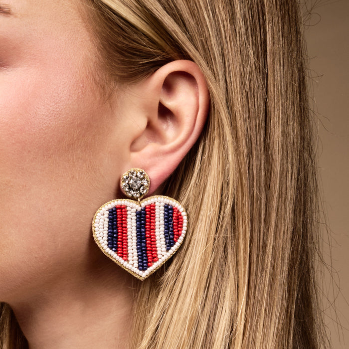 The Darling Effect’s Americana Heart Beaded Earrings feature hand-beaded red, white, and blue stripes with a gold trim, adding a playful touch to any look.