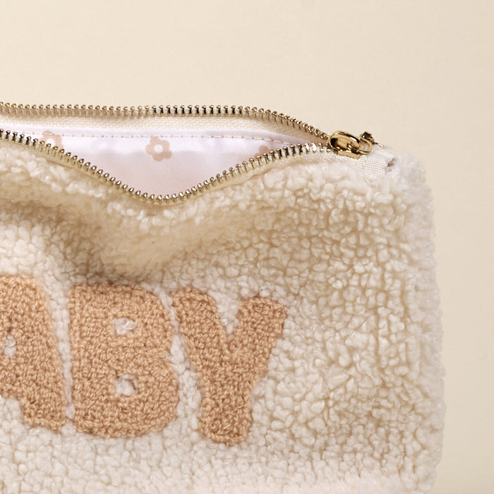 The Darling Effect’s Baby Teddy Pouch is a cream-colored sherpa pouch with “BABY” in tan chenille letters, a gold zipper, and a white lining with tiny tan flowers—an adorable addition to your teddy pouches set.
