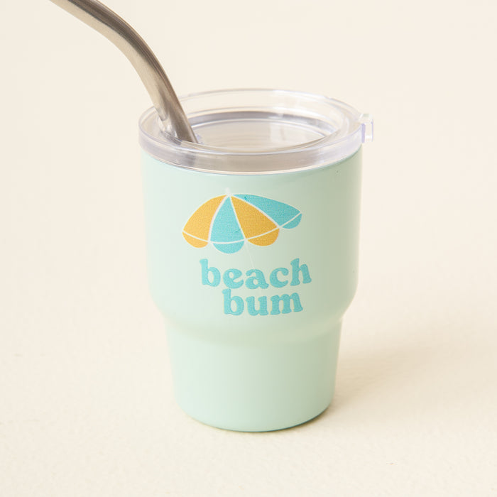 The-darling-effect Beach Bum 2 oz Tiny Tumbler: light green, insulated, with clear lid and metal straw. Features a beach umbrella illustration and “beach bum” printed on the front.