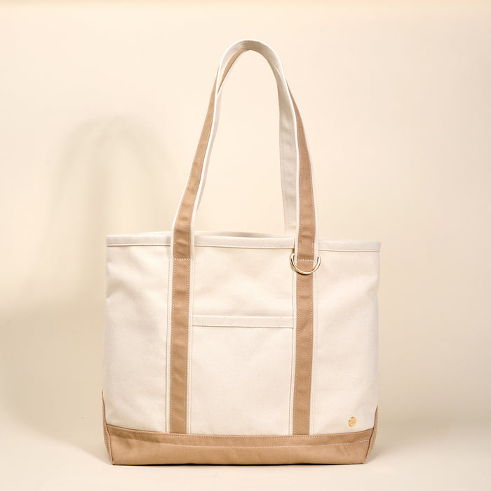 The Darling Effect's Beige The Signature Canvas Tote Bag features tan accents, a front pocket, gold D-ring on the strap, and durable handles—ideal for everyday use.