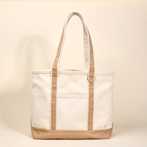The Darling Effect's Beige The Signature Canvas Tote Bag features tan accents, a front pocket, gold D-ring on the strap, and durable handles—ideal for everyday use.