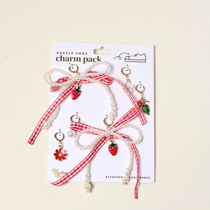 The Darling Effect’s Berry Fresh Dazzle Shoe Charm Pack includes pearl and red gingham ribbon bows, strawberry and flower sneaker charms, green leaf charms, and gold hoops—perfect for customizing your shoes. Displayed on a white backing card.