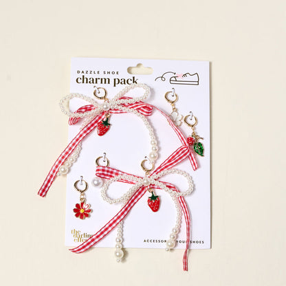 The Darling Effect’s Berry Fresh Dazzle Shoe Charm Pack includes pearl and red gingham ribbon bows, strawberry and flower sneaker charms, green leaf charms, and gold hoops—perfect for customizing your shoes. Displayed on a white backing card.