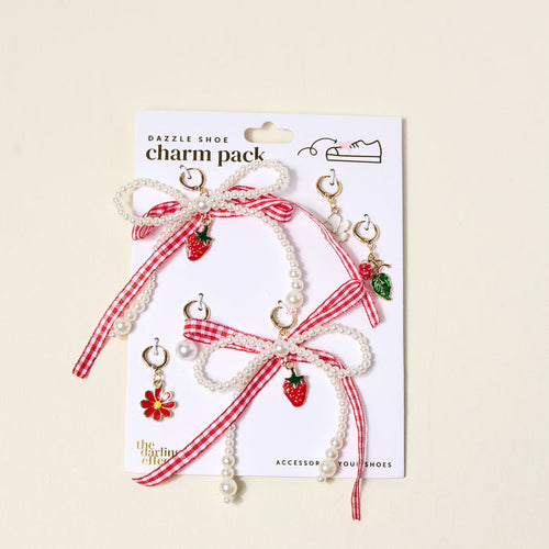 The Darling Effect’s Berry Fresh Dazzle Shoe Charm Pack includes pearl and red gingham ribbon bows, strawberry and flower sneaker charms, green leaf charms, and gold hoops—perfect for customizing your shoes. Displayed on a white backing card.