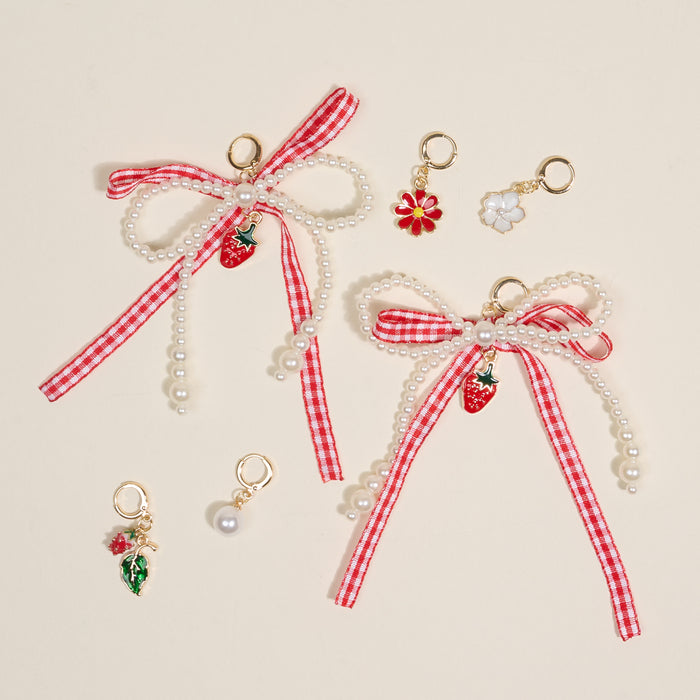 The Darling Effect’s Berry Fresh Dazzle Shoe Charm Pack includes two red and white checkered bows with pearl strands and strawberry charms, plus three smaller sneaker charms—a red flower, white flower, leaf with berries, and a single pearl.