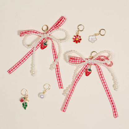 The Darling Effect’s Berry Fresh Dazzle Shoe Charm Pack includes two red and white checkered bows with pearl strands and strawberry charms, plus three smaller sneaker charms—a red flower, white flower, leaf with berries, and a single pearl.