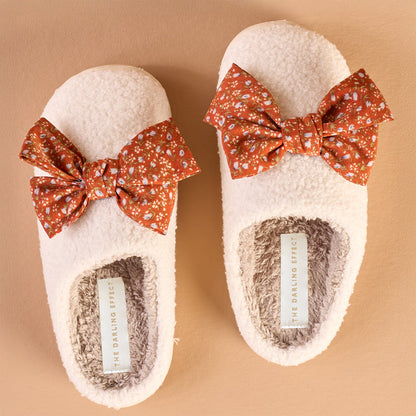 Betty Bow Fall Flora Fuzzy Slippers by The Darling Effect are fluffy white slippers decorated with orange floral bows.