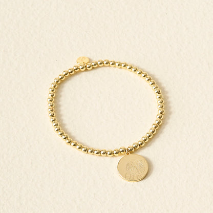 The Darling Effect's Birth Flower Beaded Charm Bracelet, featuring a round engraved pendant, rests on a light textured surface—ideal for adding a personalized touch to your jewelry collection.