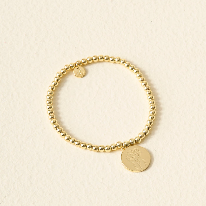 The Darling Effect Birth Flower Beaded Charm Bracelet features a gold beaded band with a round birth flower charm and a personalized initial charm.