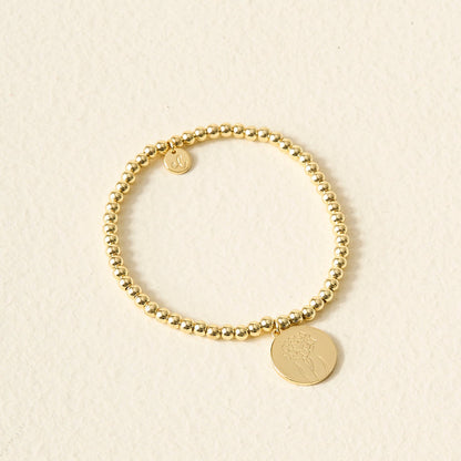 The Darling Effect Birth Flower Beaded Charm Bracelet features a gold beaded band with a round birth flower charm and a personalized initial charm.