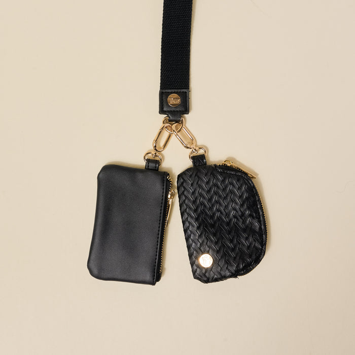 The Darling Effect’s Black Dynamic Duo Pouch Luxe Wristlet features two small black zippered pouches—one smooth leather, one woven with gold accents—attached to a chic strap for hands-free style.
