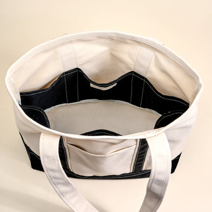 The Darling Effect Black The Signature Canvas Tote Bag features durable handles, a cream interior, black exterior accents, and multiple interior pockets and compartments for everyday use.