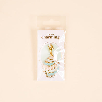 The Darling Effect’s Blue Shell Beauty Jewelry Charm Gold, shaped like a seashell with turquoise enamel, is shown in clear packaging labeled “Oh So Charming” against a pale background.